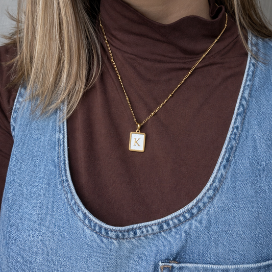 Close-up of a person wearing a gold necklace with a square pendant.