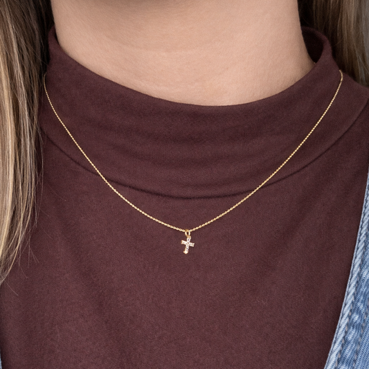 Gold necklace with a cross pendant worn by a person in a brown top.