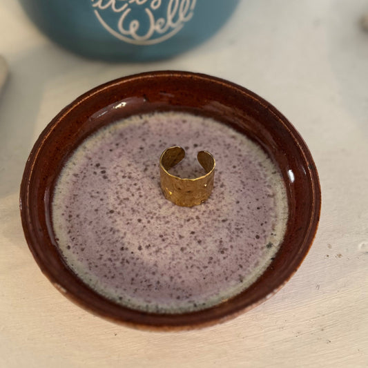Ceramic dish with a gold ring on a speckled surface, with a blue mug in the background.