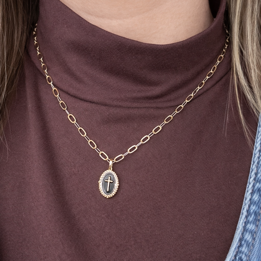 Gold necklace with a pendant on a person wearing a brown top.