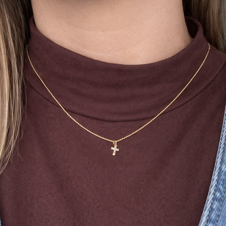 Gold necklace with a cross pendant worn by a person in a brown top.