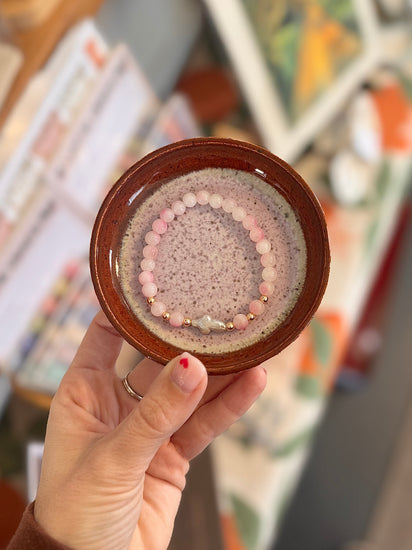 Hand holding a small round dish with a bracelet on a blurred background