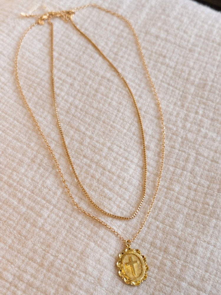Gold necklace with a pendant on a textured beige surface